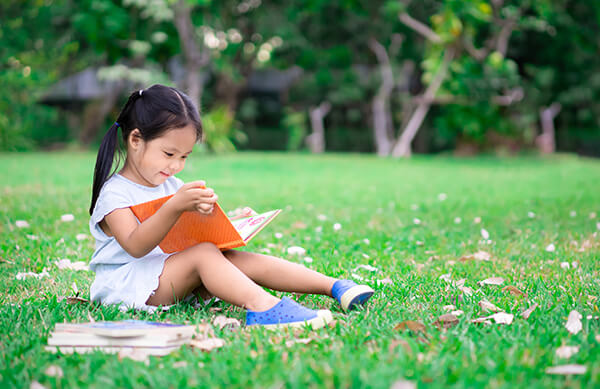 Small girl reading book outside 