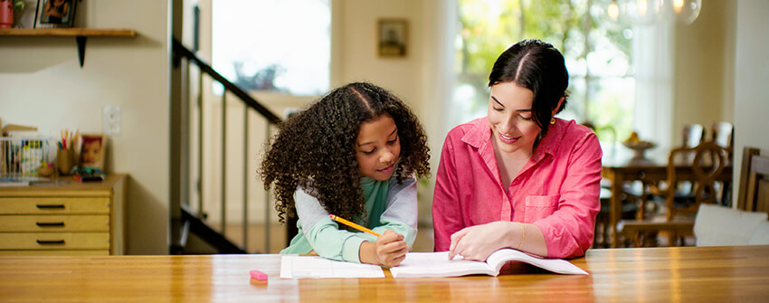 Mother sitting at table helping her daughter who is struggling with learning loss Mother sitting at table helping her daughter who is struggling with learning loss