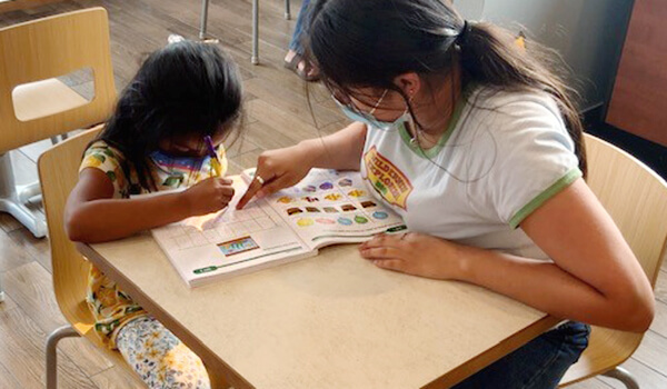 Teacher helping student with activity in Summer Bridge Activities workbook