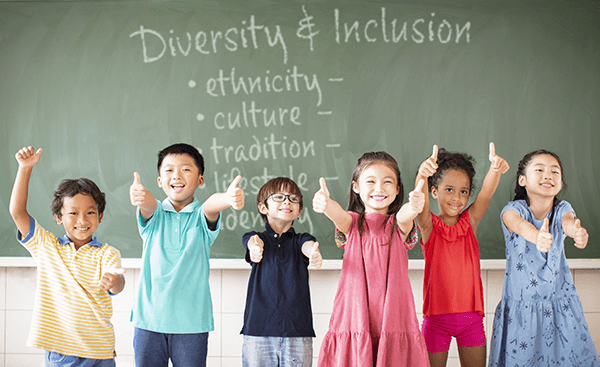 Children standing in front of chalkboard excited to learn about diversity and inclusion